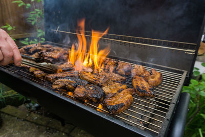 Cropped hand preparing meat on barbecue grill