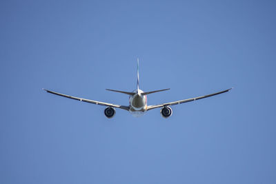 Low angle view of airplane flying against clear blue sky