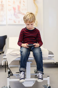 Boy using smart phone on examination table in orthopedic clinic