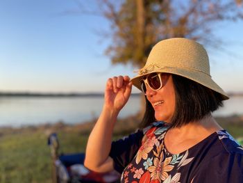Smiling mature woman wearing hat standing outdoors during sunset