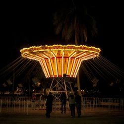 People in illuminated amusement park against sky at night