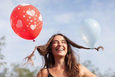 Happy woman tied balloons in hair against sky