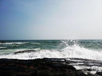 Sea waves splashing on shore against sky