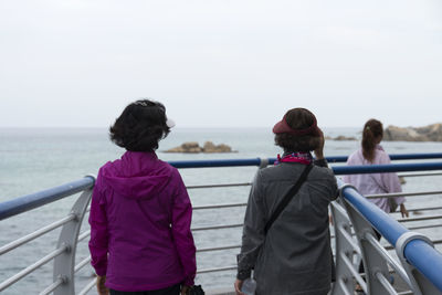 Rear view of friends walking on footbridge against clear sky