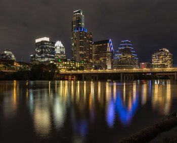 Illuminated buildings by river against sky at night