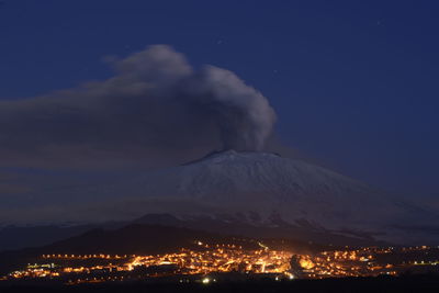 Aerial view of illuminated cityscape against sky at night and etna eruption