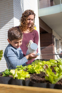 Mother and son watering vegetables in their urban garden