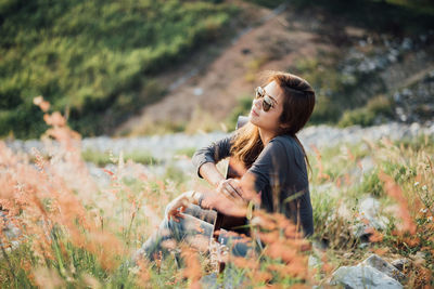 Woman with guitar sitting on field