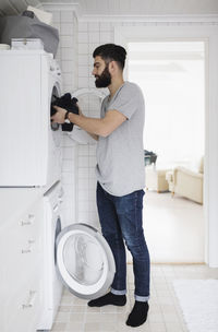 Side view of man loading clothes in washing machine at home