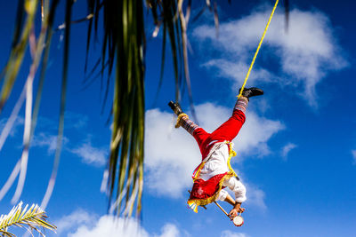 Low angle view of man hanging against blue sky