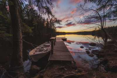 Boat moored on lake against sky during sunset