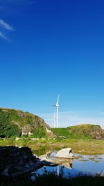 Windmills on lake against clear blue sky