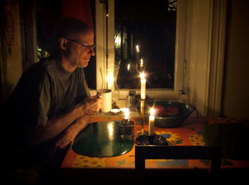 Smiling mature man having tea on illuminated dining table at home