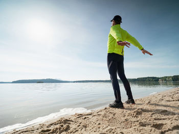 Sportsman stretching shoulders and back on lake shore. early morning outdoor workout.