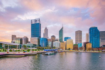 Modern buildings by river against sky in city