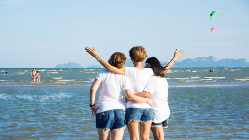 Rear view of friends standing on beach against sky