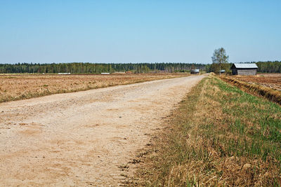 Road passing through agricultural field against clear sky