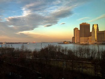 Sea by city buildings against sky during sunset