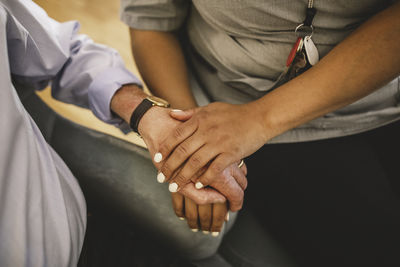 Midsection of young female nurse holding hands while consoling senior man at retirement home