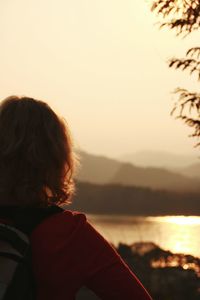 Rear view of woman sitting against sea during sunset