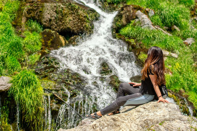 Woman sitting on rock by waterfall