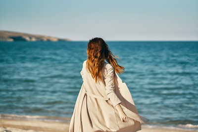 Rear view of woman standing by sea against sky