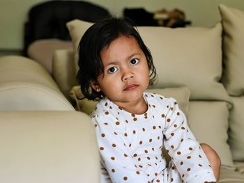 Portrait of cute girl sitting on sofa at home