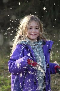 Portrait of girl playing with dandelion seeds on field