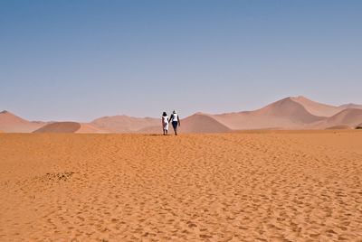 Tourists on sand dune against clear sky