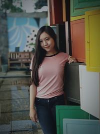 Portrait of smiling young woman standing against door