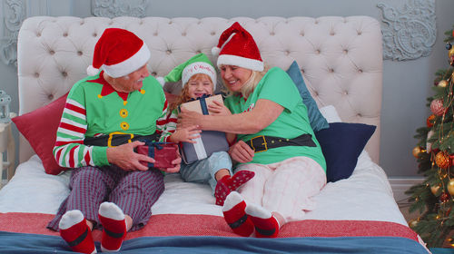 Smiling grandparents giving gift to granddaughter sitting on bed