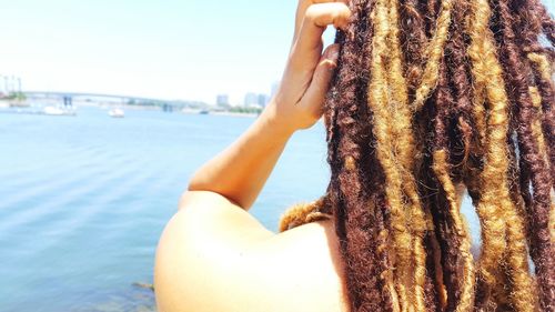 Rear view of woman with dreadlocks standing by sea against clear sky