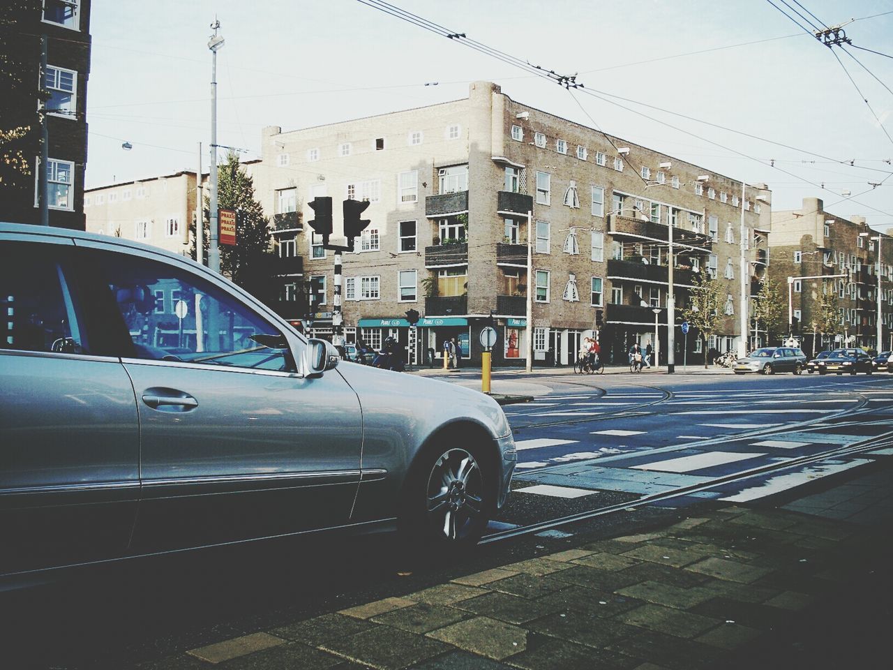 transportation, building exterior, mode of transport, architecture, built structure, car, land vehicle, city, street, road, building, city street, window, travel, day, on the move, road marking, clear sky, sky, street light