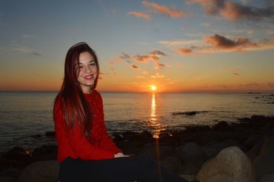 Beautiful young woman sitting on beach during sunset