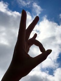 Low angle view of cropped hand against cloudy sky