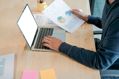 Midsection of businessman analyzing data while working at laptop on table in office 