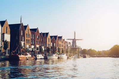 Sailboats moored on river by buildings against clear sky