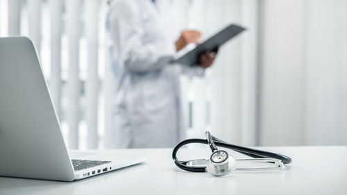 Midsection of doctor writing on clipboard