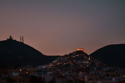 Illuminated buildings in town against sky at night