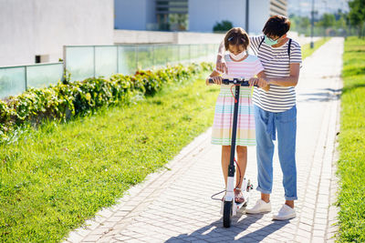 Full length of mother and daughter wearing mask standing on footpath