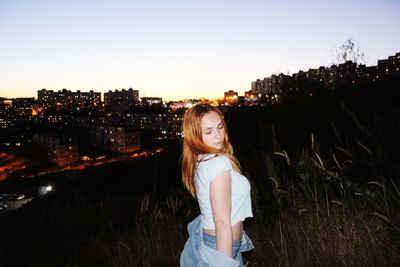 Portrait of young woman standing against sky in city