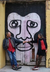 Full length portrait of man standing against graffiti wall