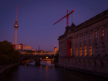 Illuminated bridge over river by buildings in city