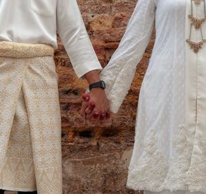 Midsection of bride and groom holding hands against wall