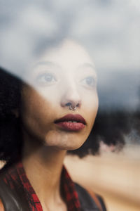 Thoughtful woman with nose pierced seen through glass