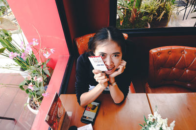 Portrait of young woman using phone while sitting on potted plant