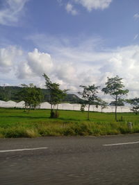 Road by trees on field against sky