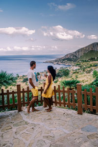 Rear view of friends standing on shore against sky