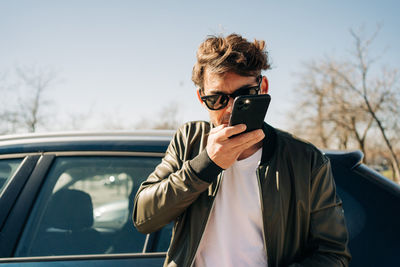 Portrait of man holding camera while standing by car