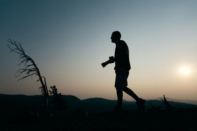 Silhouette of man holding camera at sunset
